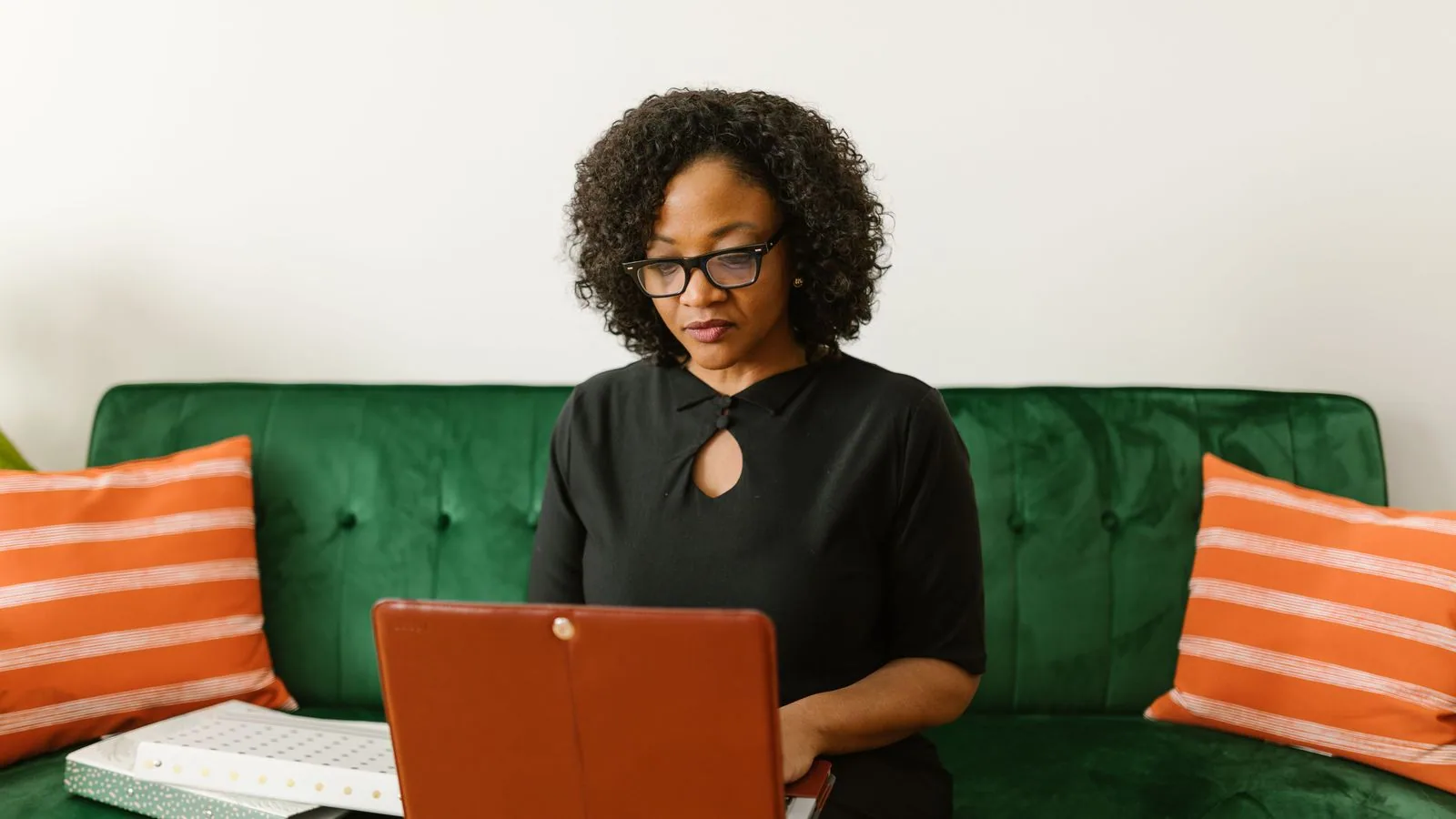 A woman working on a laptop while seated on a green sofa
