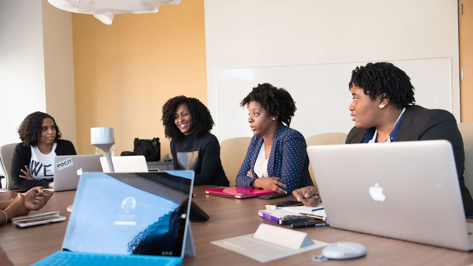 Four women working together around a table with laptops