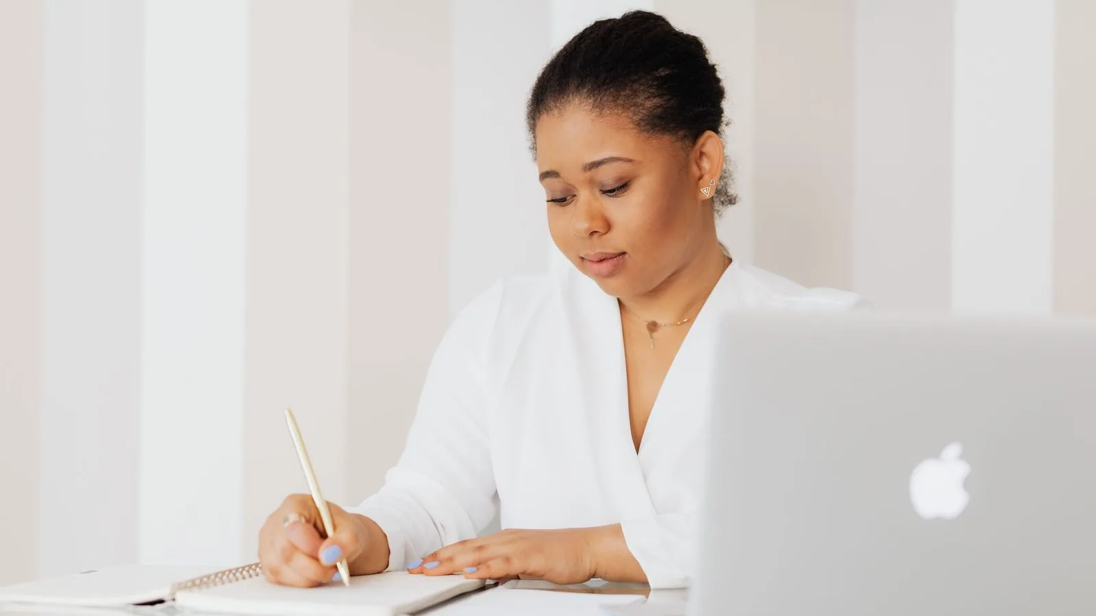 A woman writing notes beside a laptop