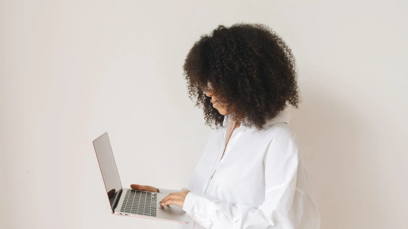A woman using a laptop while standing beside a window