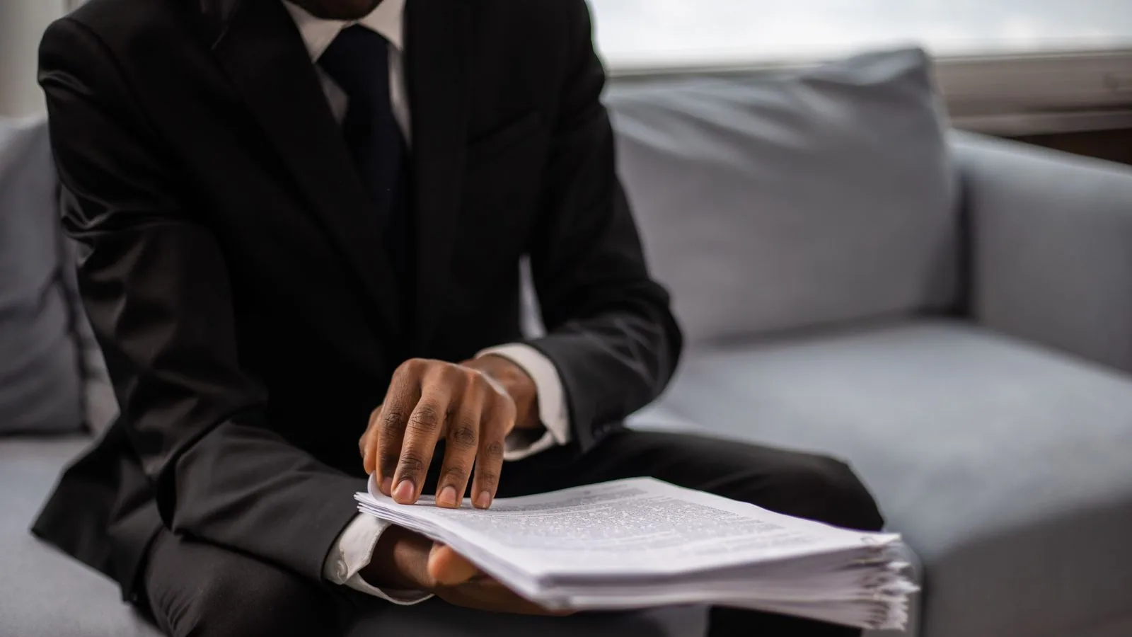 A person reviewing printed documents while seated on a sofa