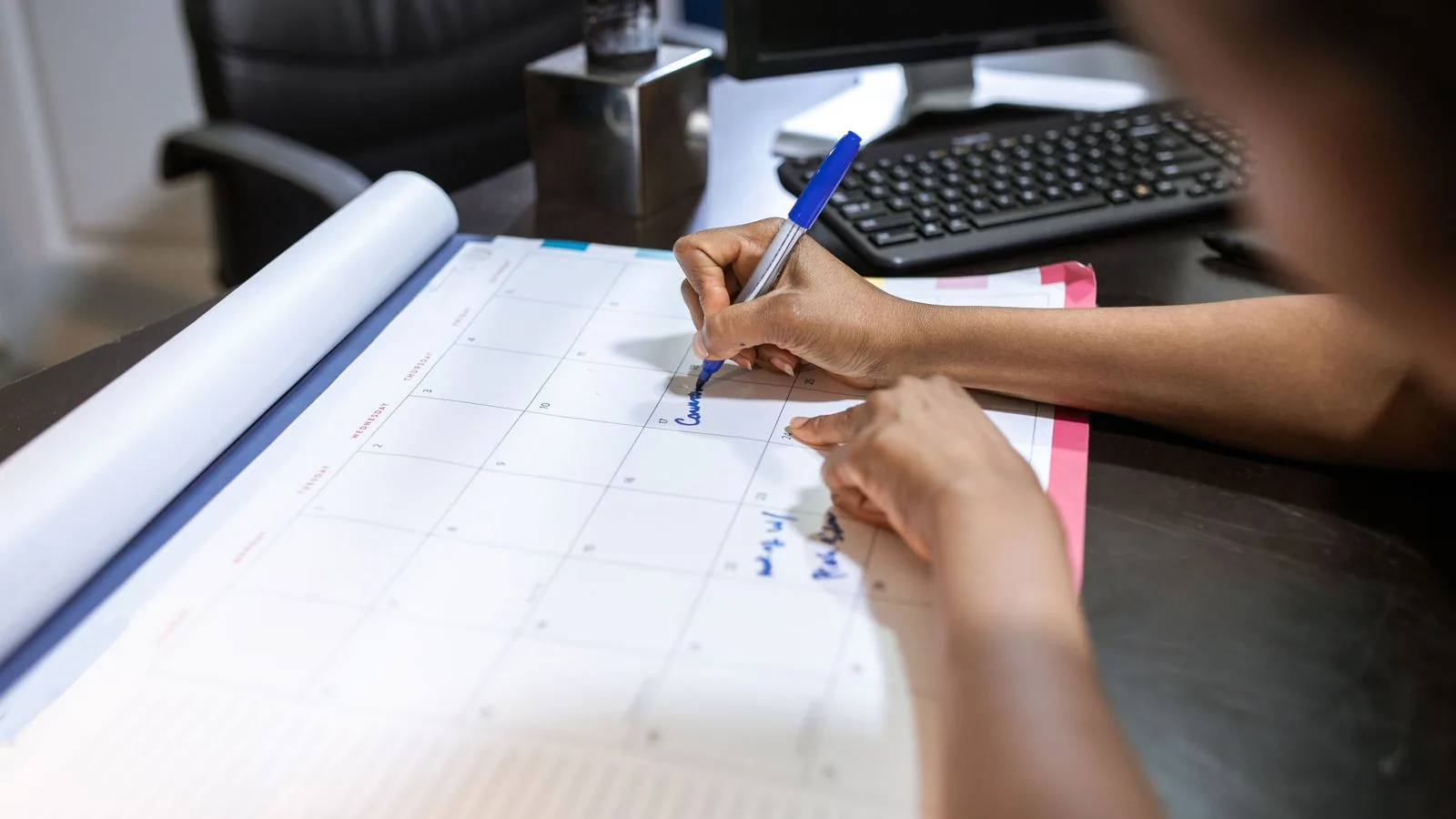 Hands writing appointments on a desk calendar