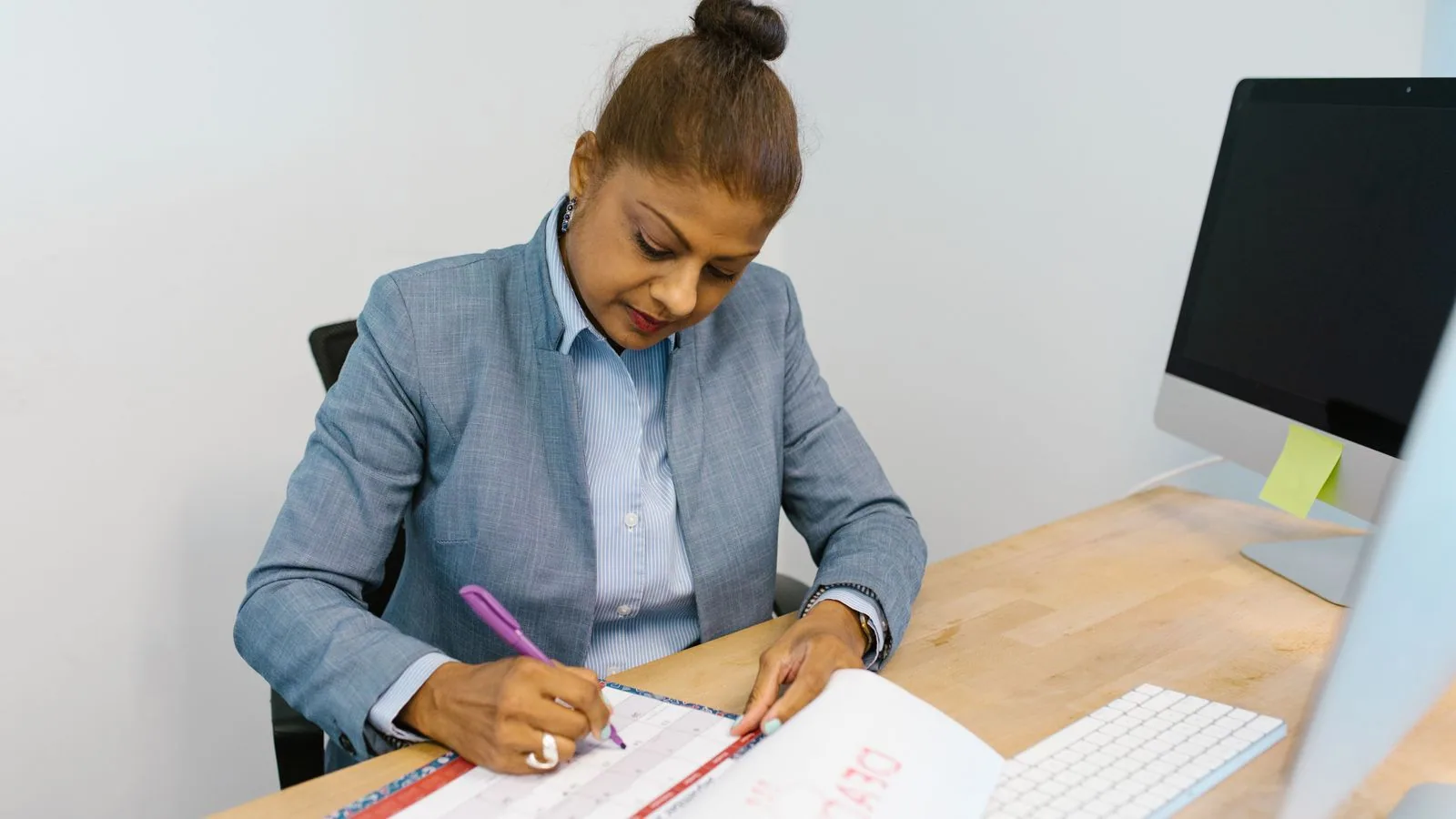 A woman writing in a planner beside her computer