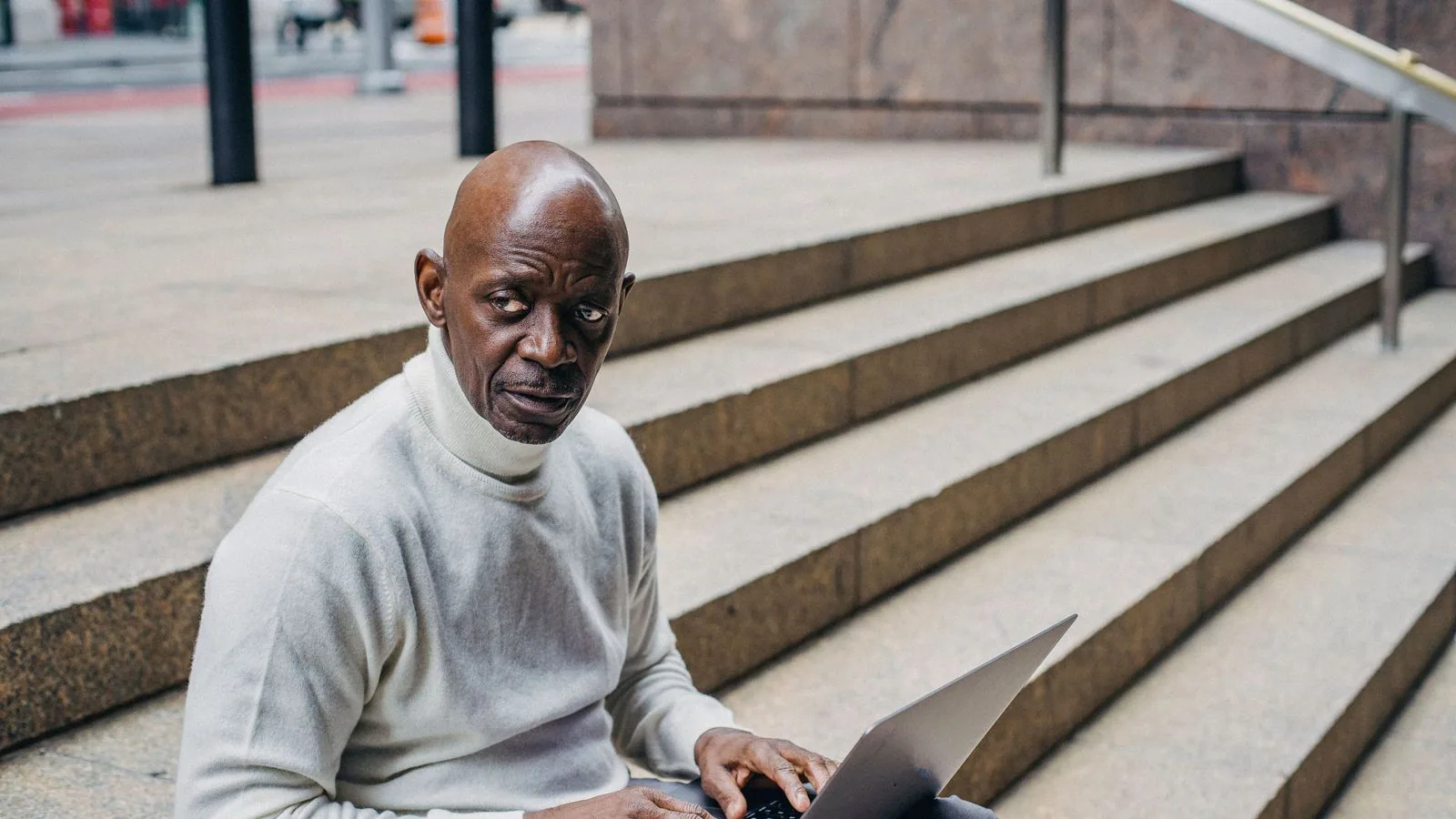 A man using a laptop while seated on outdoor steps