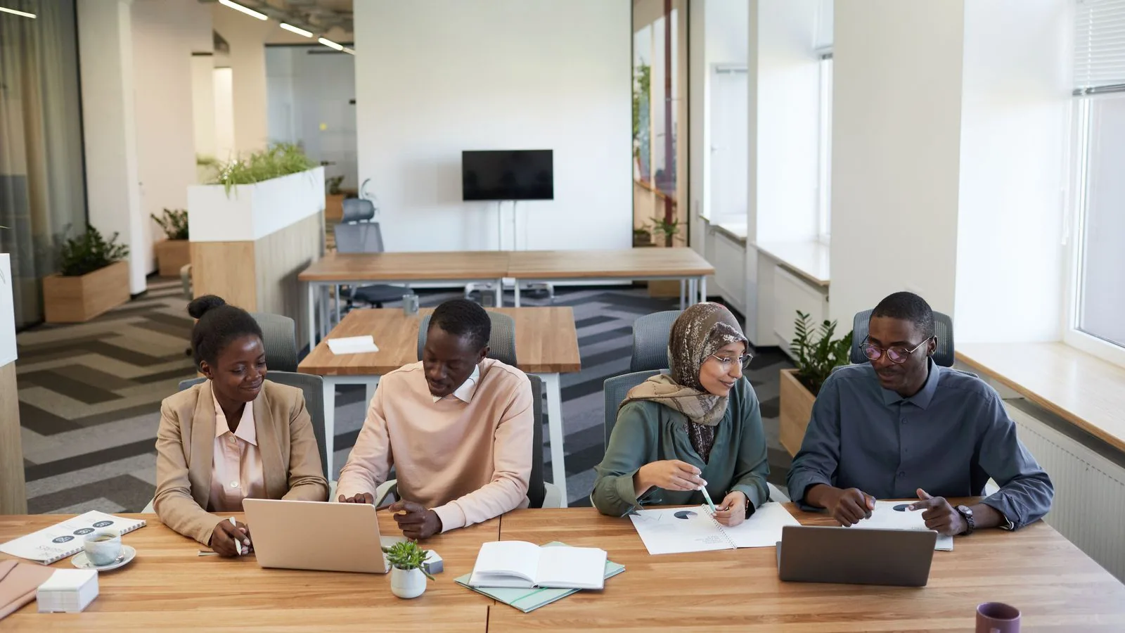 Four colleagues reviewing paperwork and laptops at a table