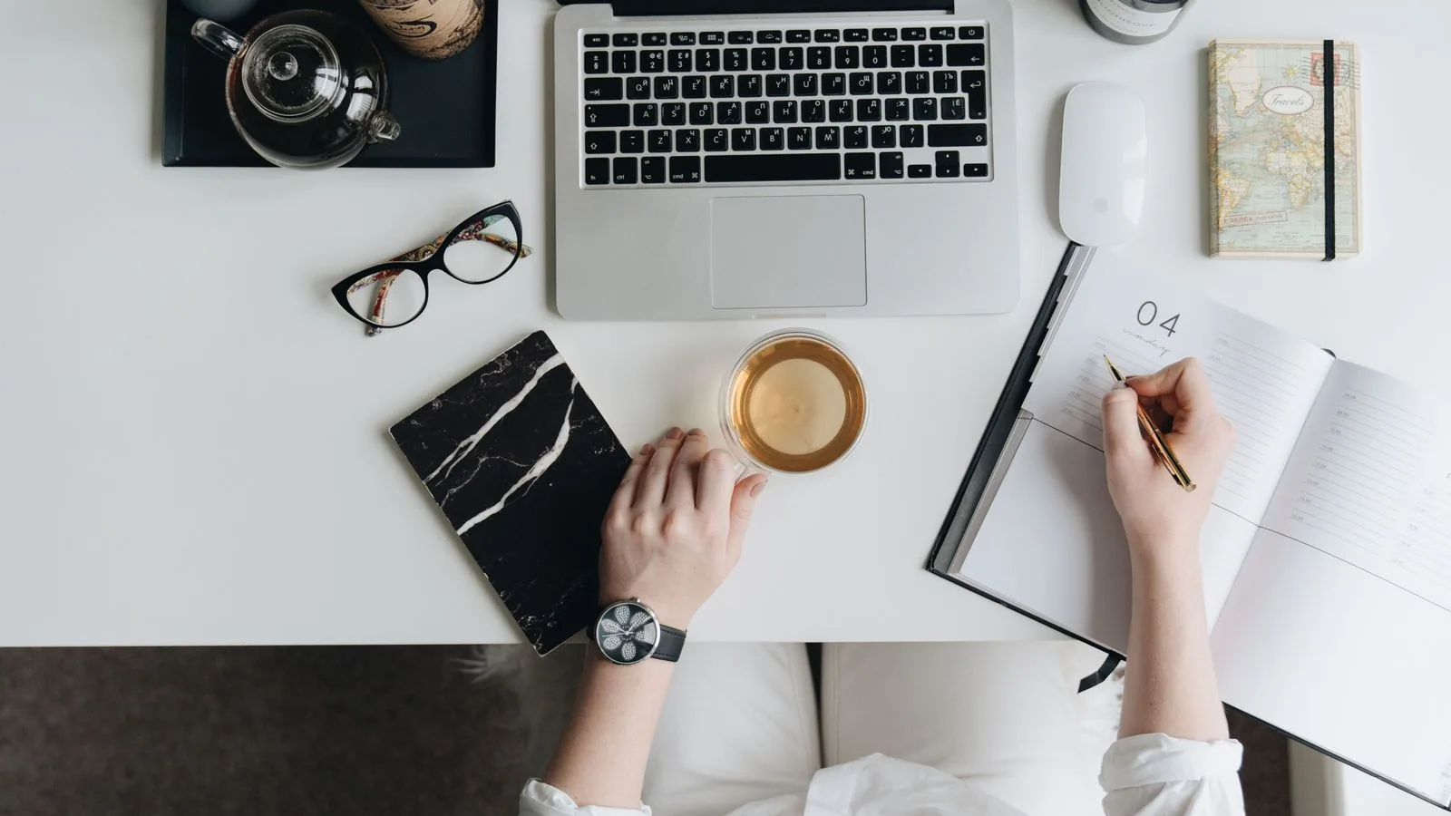 An overhead view of a laptop, notebook, glasses and coffee