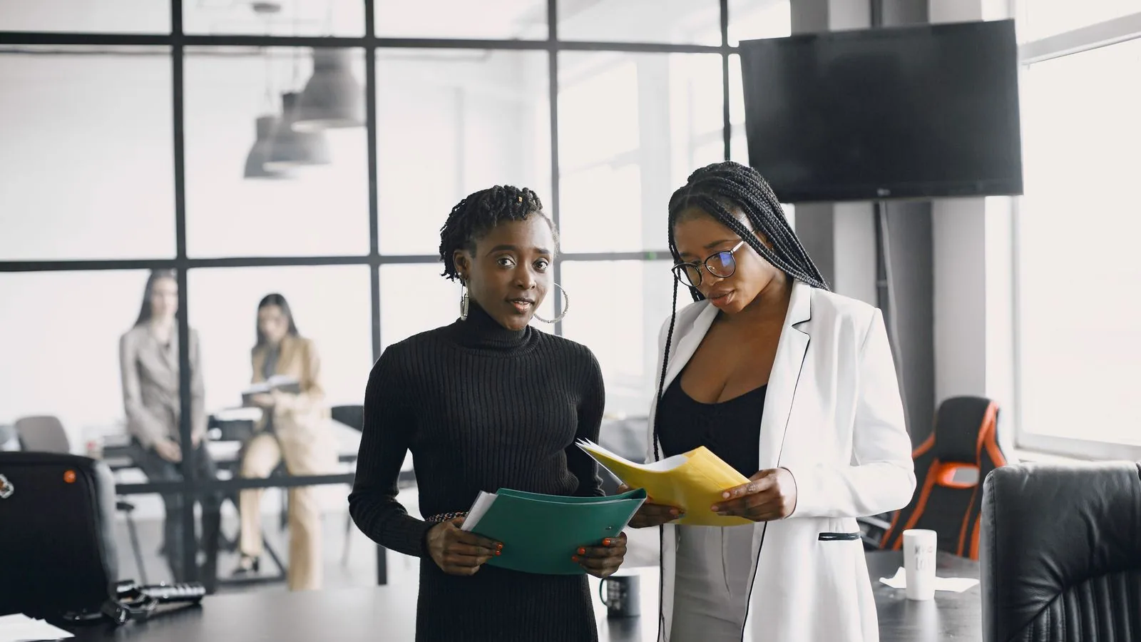 Two women comparing document folders in an office