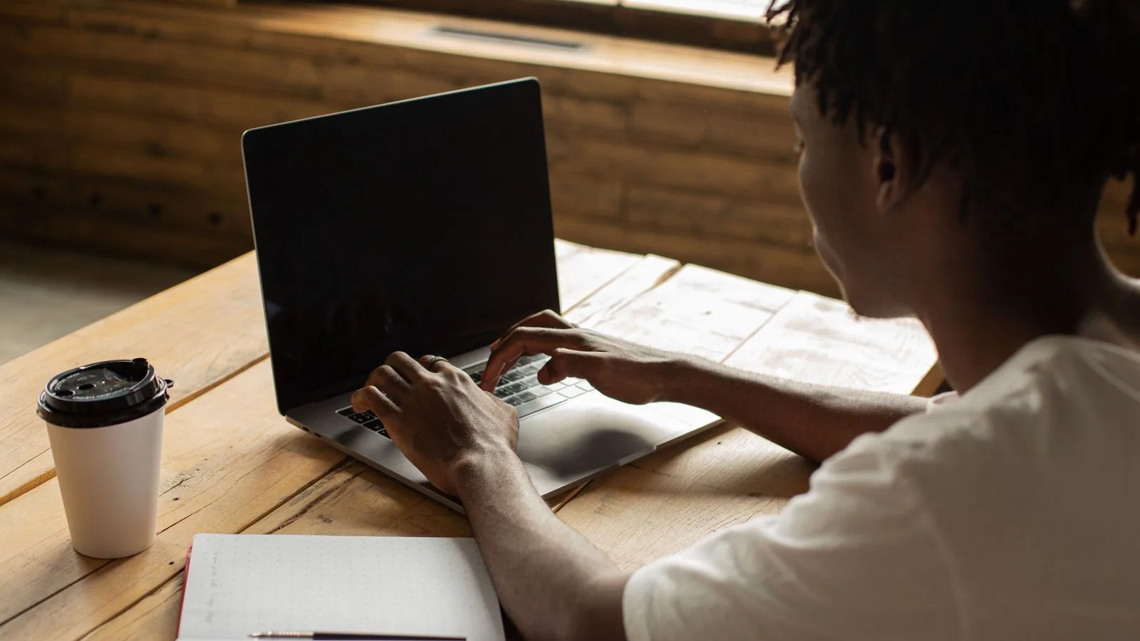 A person using a laptop beside coffee and a notebook