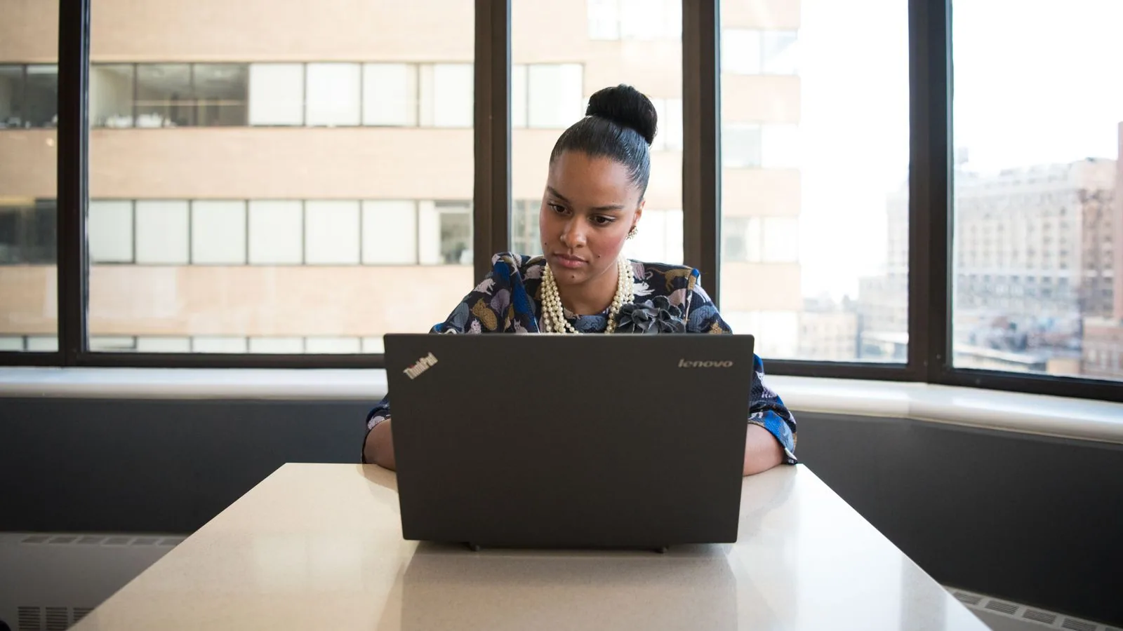 A woman working at a laptop beside large office windows