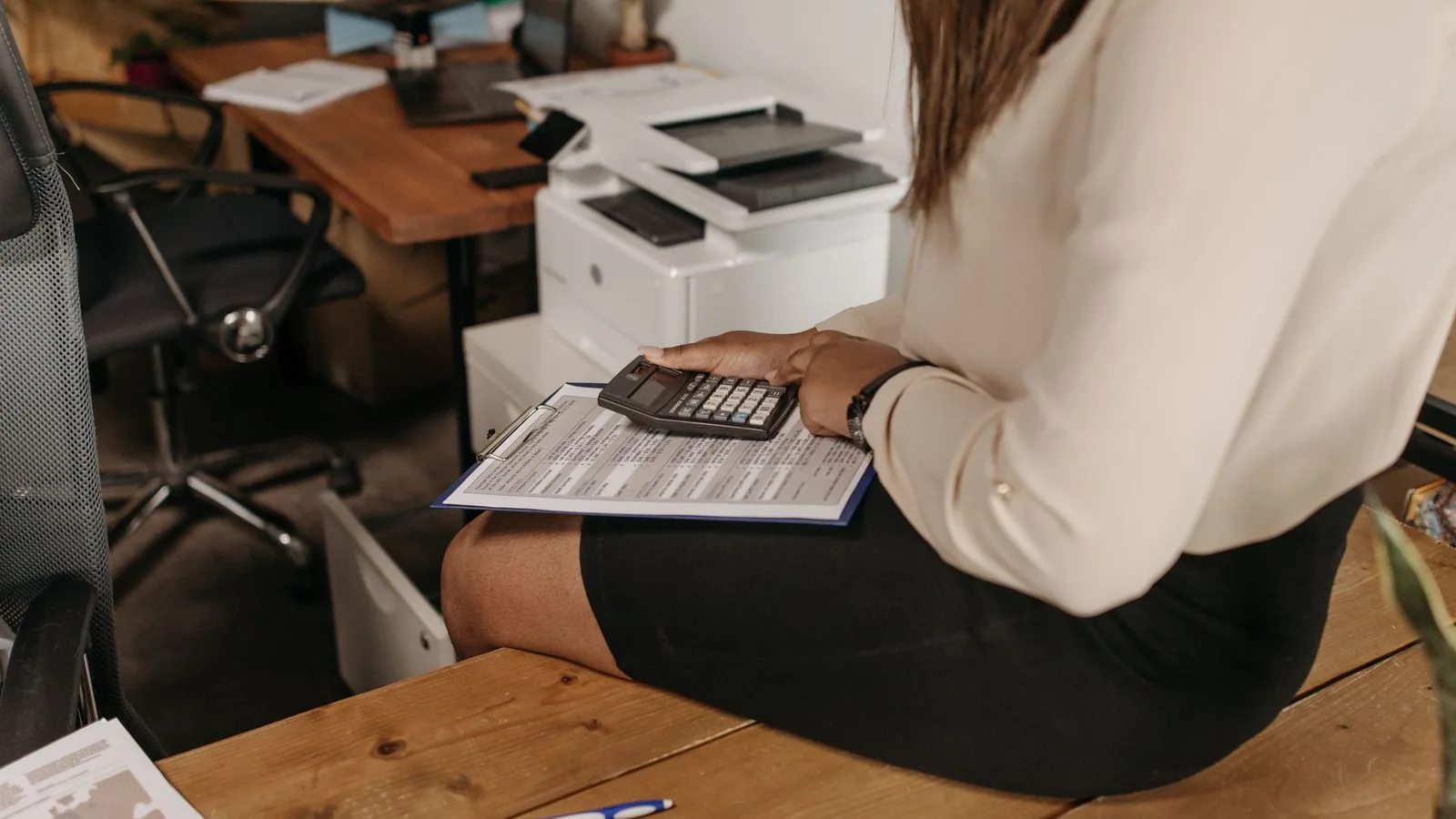 A woman calculating figures on a clipboard beside office equipment