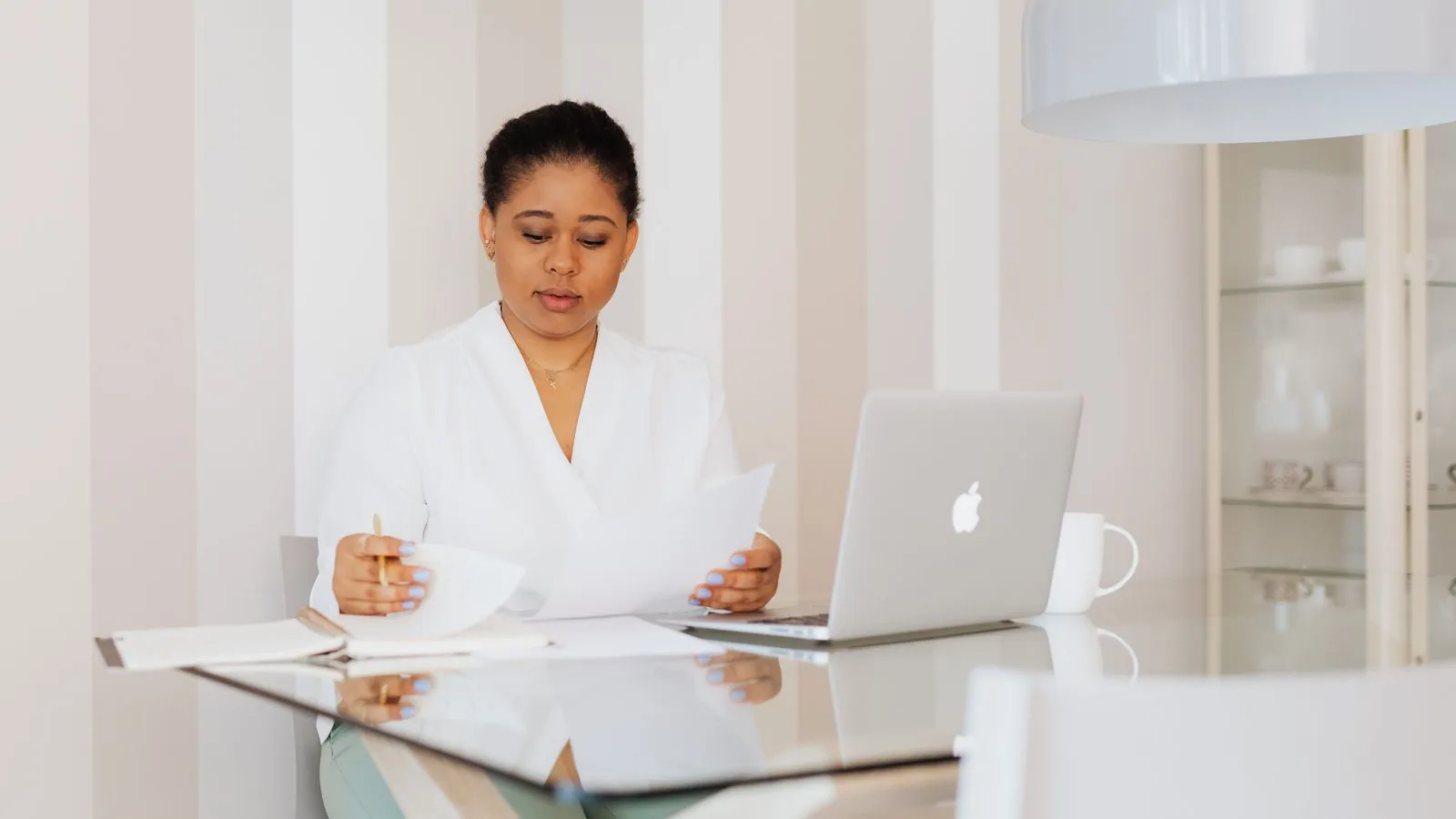 A woman reading paperwork at a desk beside a laptop
