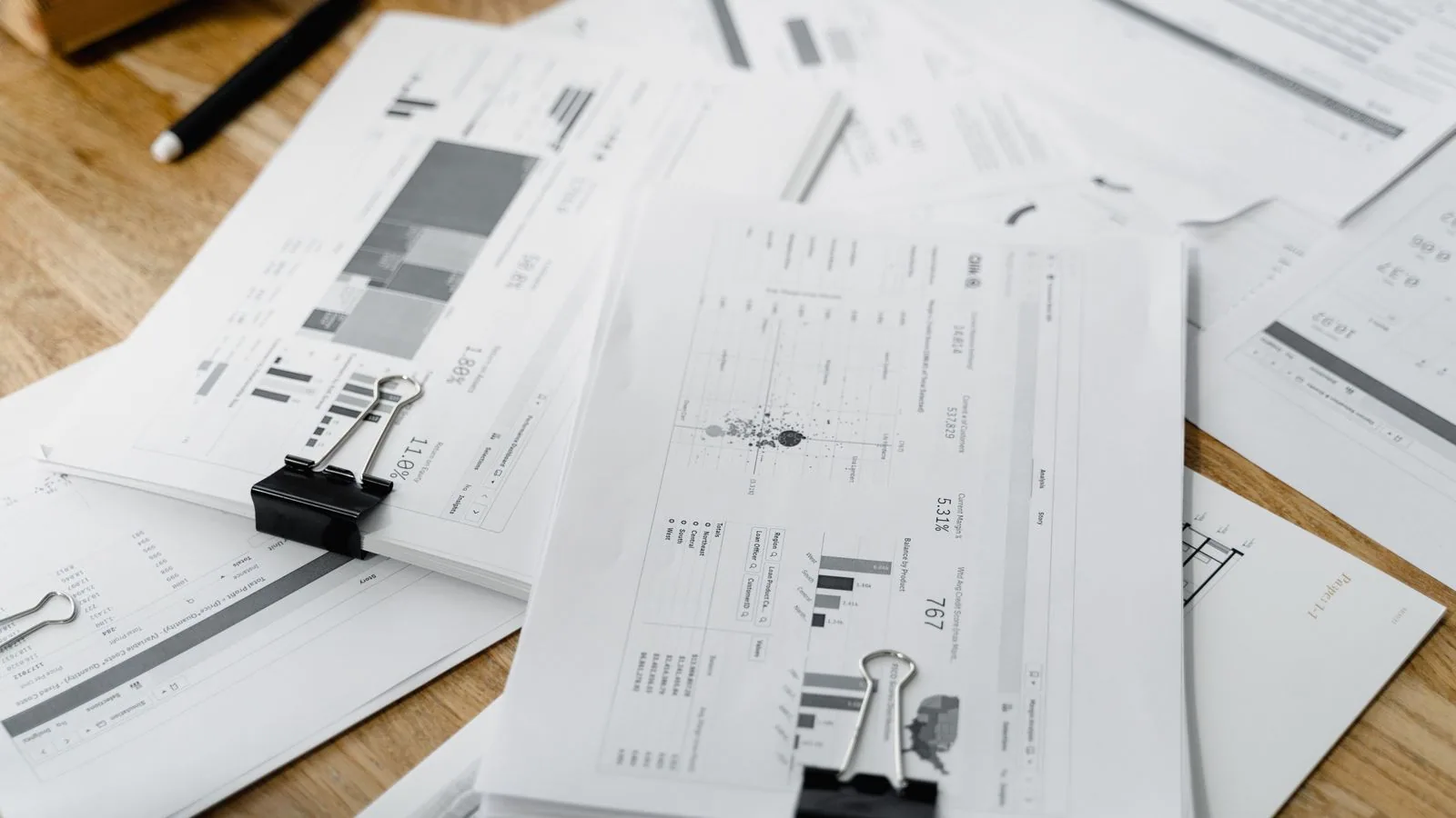 Printed financial charts clipped together on a wooden desk