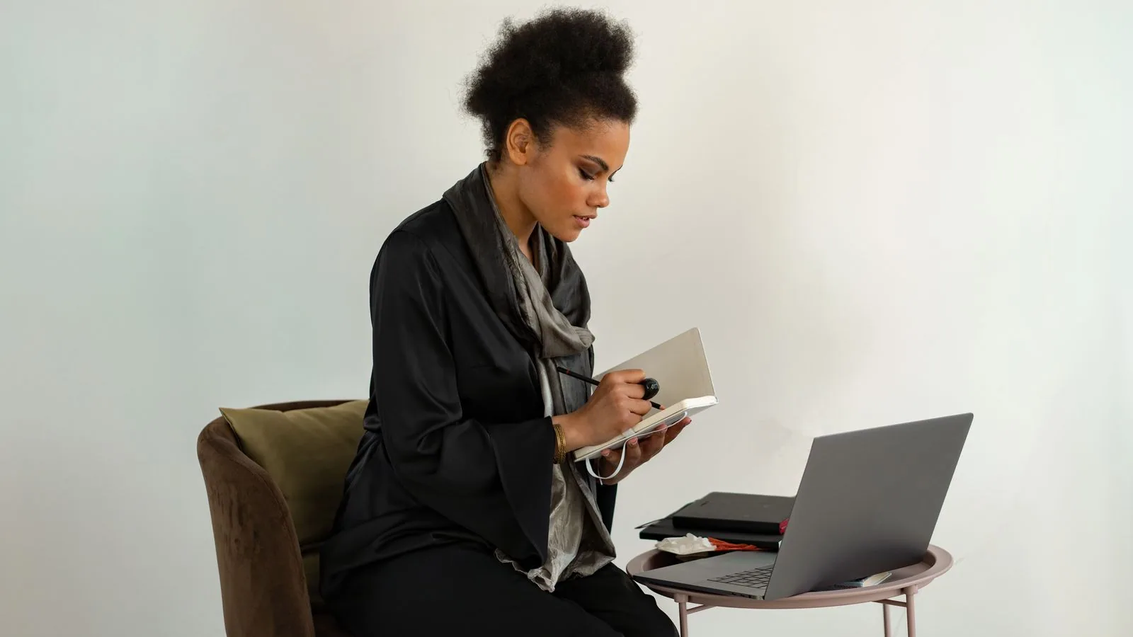 A woman checking a notebook beside her laptop