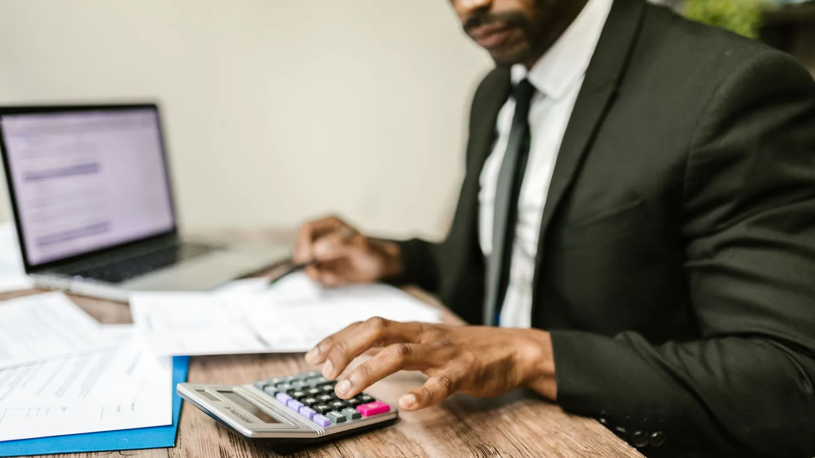 A person checking paperwork with a calculator at a desk