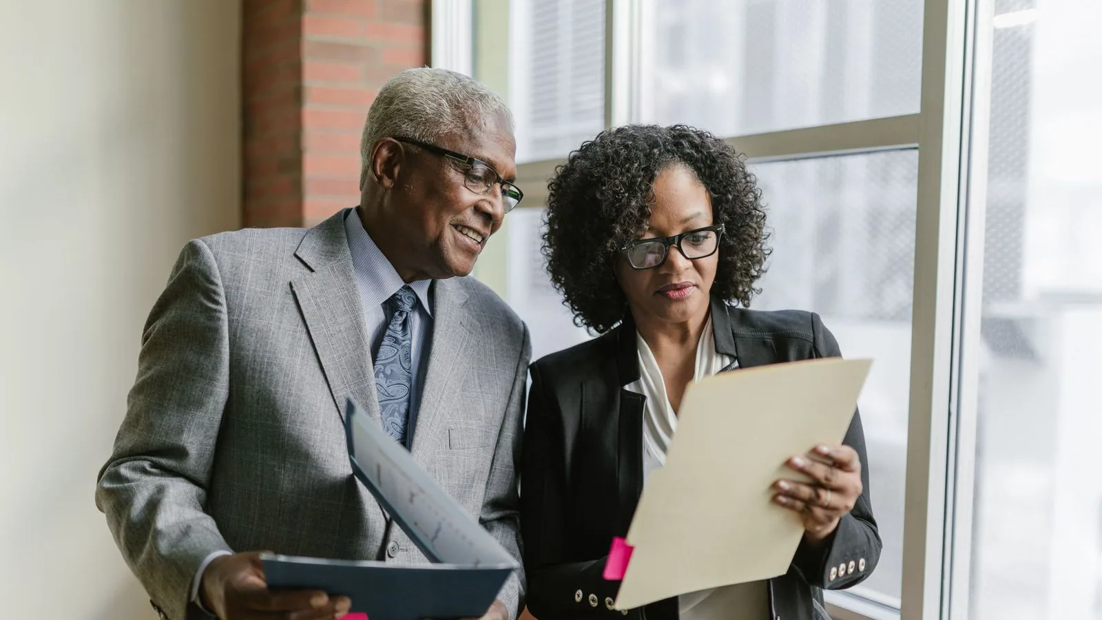 Two businesspeople comparing a tablet with printed paperwork