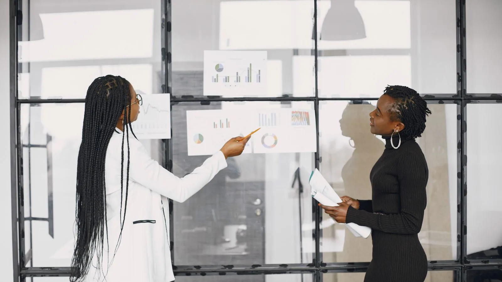 Two women comparing charts on an office whiteboard