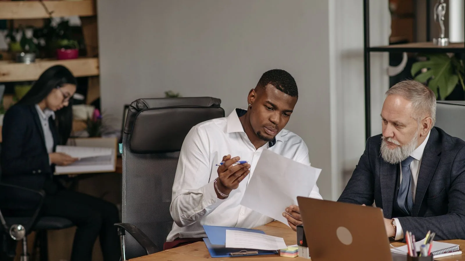Three colleagues comparing paperwork beside a laptop