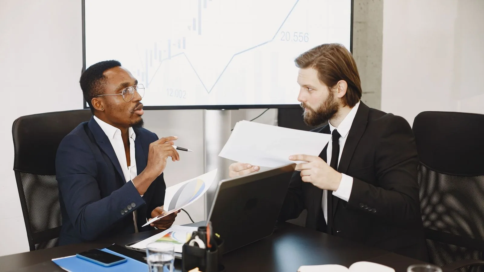 Two businesspeople discussing papers at a meeting table